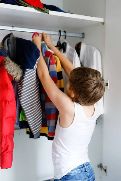 School kid boy standing by wardrobe with clothes. Child making decision for school shirt to wear. Children get dressed in the morning for school. — Stock Photo, Image