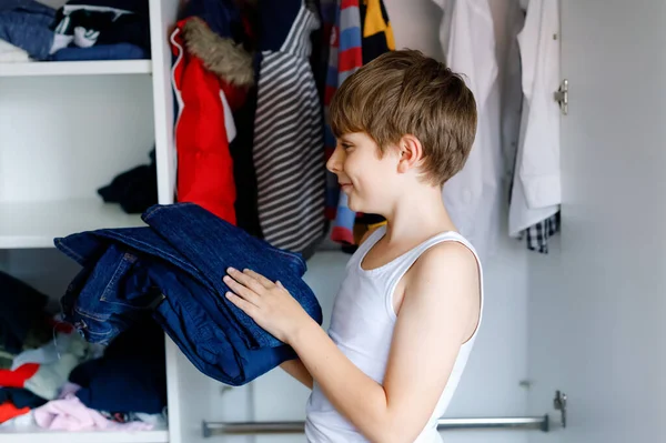 Niño de la escuela de pie junto al armario con ropa. Niño tomando la decisión de pantalones vaqueros de la escuela para usar. Los niños se visten por la mañana para ir al colegio. — Foto de Stock