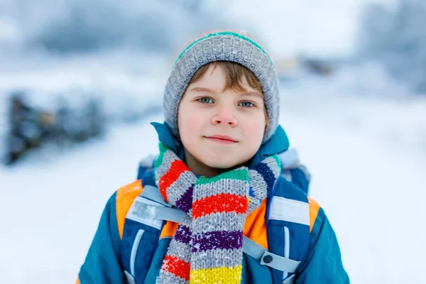 Gorgeous little school kid boy of elementary class walking to school during strong snowfall. Early morning and snowy streets in city. Child with backpack or satchel in colorful winter clothes — Stock Photo, Image