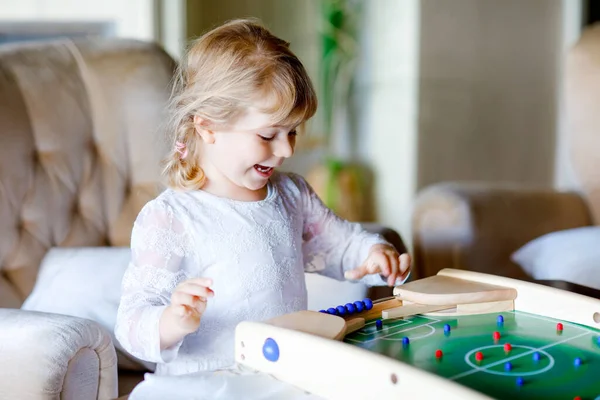 Menina pequena feliz jogando futebol de mesa com a família em casa. Criança sorrindo ganhando futebol de bordo, dentro de casa. Lazer interno para crianças durante o tempo de quarentena auto-isolamento do vírus da corona. — Fotografia de Stock