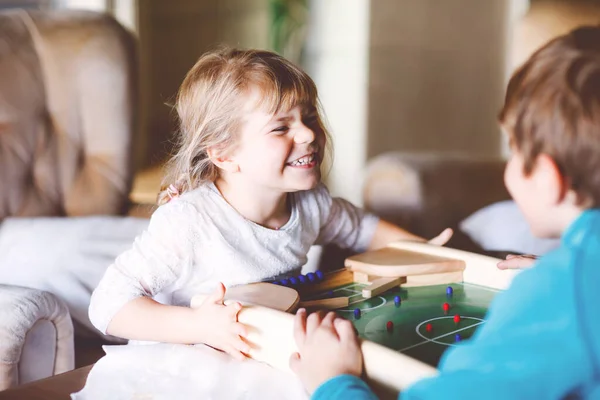 Peuter meisje en kind jongen spelen tafelvoetbal met familie thuis. Lachende kinderen, broers en zussen spelen bordvoetbal, binnen. Indoor vrije tijd voor kinderen tijdens corona virus zelf-isolatie quarantaine tijd. — Stockfoto