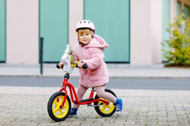 Kask takıp kreşe, çocuk parkına ya da çocuk parkına giden dengeli bisiklete binen tatlı küçük kız. Mutlu çocuk bisiklet sürerek öğrenirken eğleniyor. Soğuk bir sonbahar gününde açık havada hareketli bir çocuk..