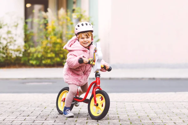 Jolie petite fille tout-petit avec casque d'équitation sur vélo d'équilibre de course à la garderie, école de jeux ou jardin d'enfants. Enfant heureux s'amuser avec l'apprentissage sur vélo apprenant. Enfant actif lors d'une froide journée d'automne en plein air. — Photo