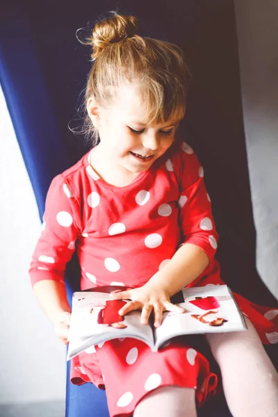 Pequena criança elegante menina ler e olhar revista de moda ou catálogo. Criança adorável se divertindo com a escolha de roupas. — Fotografia de Stock