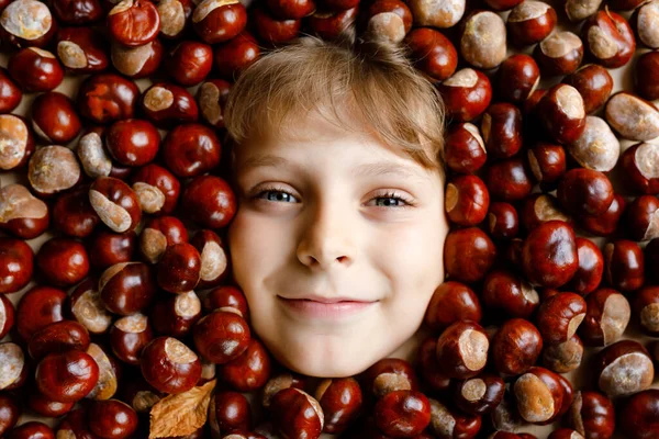 Divertente ritratto di preadolescente o ragazzo della scuola con un sacco di castagne. Sorridente bambino felice divertirsi nella giornata autunnale con un progetto scolastico. — Foto Stock