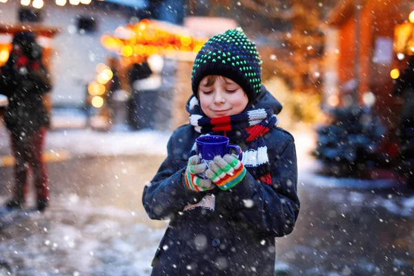 Pequeno menino bonito bebendo crianças quentes soco ou chocolate no mercado de Natal alemão. Criança feliz no mercado familiar tradicional na Alemanha, menino rindo em roupas coloridas de inverno — Fotografia de Stock