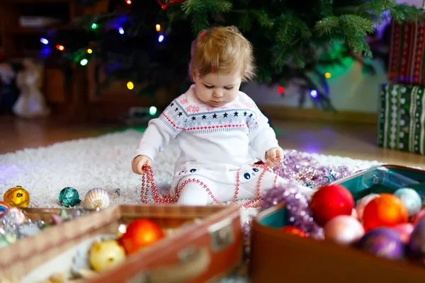 Schattige baby meisje met kleurrijke lichten bloemenslinger in schattige handen. Klein kind in feestelijke kleding versieren kerstboom met familie. Eerste viering van de traditionele feestdag genaamd Weihnachten — Stockfoto