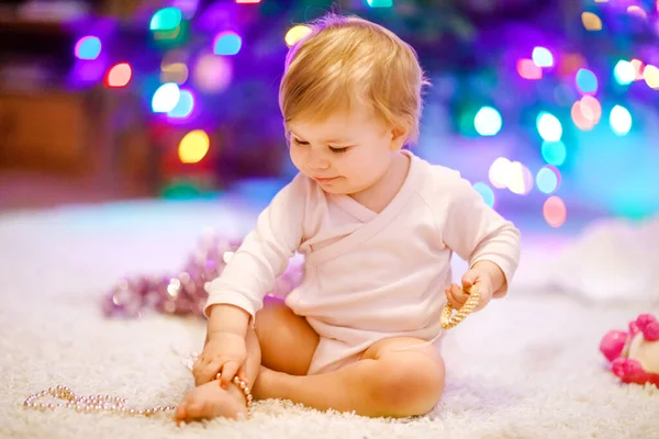 Adorabile bambina che tiene ghirlanda luci colorate in mani carine. Bambino in abiti festivi che decorano l'albero di Natale con la famiglia. Prima celebrazione della festa tradizionale chiamata Weihnachten — Foto Stock