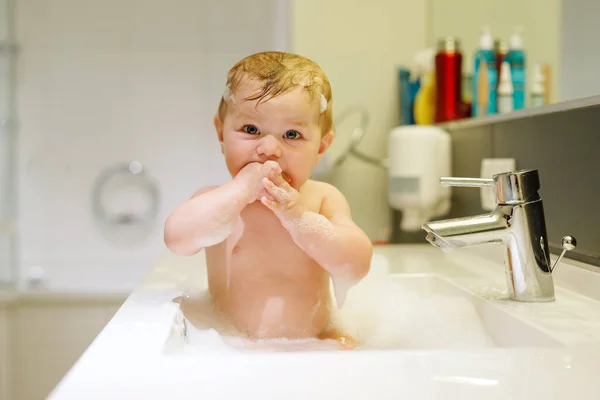 Lindo bebé adorable tomando baño en lavabo y jugando con agua y espuma —  Fotos de Stock