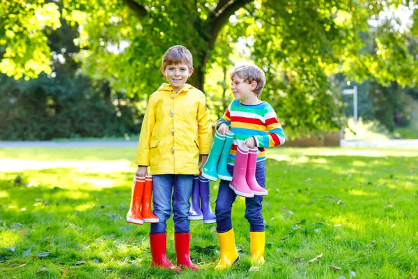 Due bambini piccoli ragazzi, fratelli carini con un sacco di stivali da pioggia colorati. Bambini in diversi stivali e giacche di gomma. Calzature per caduta piovosa. Gemelli sani e migliori amici si divertono all'aperto — Foto Stock