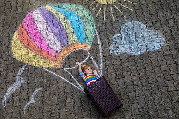 Felice bambina che vola in mongolfiera dipinta con gessetti colorati in colori arcobaleno a terra o asfalto in estate. Bel bambino che si diverte. svago creativo per bambini. — Foto Stock