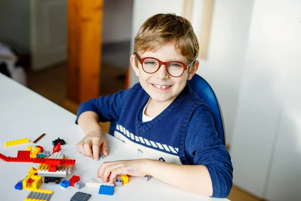 Petit enfant blond avec des lunettes jouant avec beaucoup de blocs en plastique coloré. Adorable écolier qui s'amuse avec la construction et la création de robots. Loisirs créatifs technique moderne et robotique. — Photo