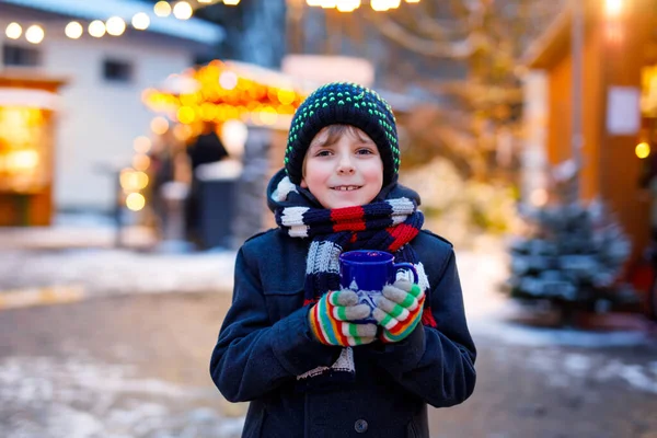 Petit garçon mignon qui boit du punch ou du chocolat chaud pour enfants sur le marché de Noël allemand. Enfant heureux sur le marché familial traditionnel en Allemagne, Rire garçon en vêtements d'hiver colorés — Photo