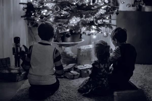 Zwei kleine Jungen und ein entzückendes Kleinkind sitzen am Weihnachtsbaum mit altem Spielzeug und Kugeln mit vielen Geschenken an Heiligabend. Familienvorbereitungsfeier zum Familienfest — Stockfoto