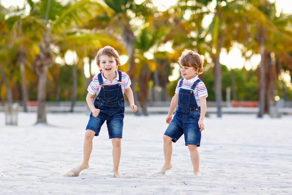 Two little kids boys having fun on tropical beach, happy best friends playing, friendship concept. Siblings brothers, twins in family look with palms trees on background. Family vacations. — Stock Photo, Image