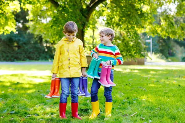 Duas crianças meninos, irmãos bonitos com muitas botas de chuva coloridas. Crianças em diferentes botas de borracha e jaquetas. Calçado para queda chuvosa. Gêmeos saudáveis e melhores amigos se divertindo ao ar livre — Fotografia de Stock