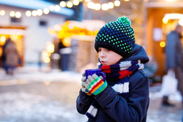 Little cute kid boy drinking hot children punch or chocolate on German Christmas market. Happy child on traditional family market in Germany, Laughing boy in colorful winter clothes — Stock Photo, Image