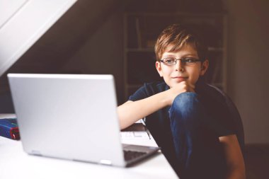 Gözlüklü çocuk evde okulda laptopta öğreniyor. Ev ödevi yapan, defter ve modern aletler kullanan sevimli bir çocuk. Evde eğitim kavramı.