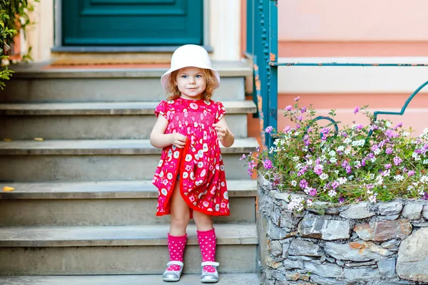 Portrait de belle petite gorgée belle jeune fille en rose look d'été vêtements, robe de mode, chaussettes de genou et chapeau. Bébé enfant heureux et en bonne santé posant devant la maison colorée. — Photo