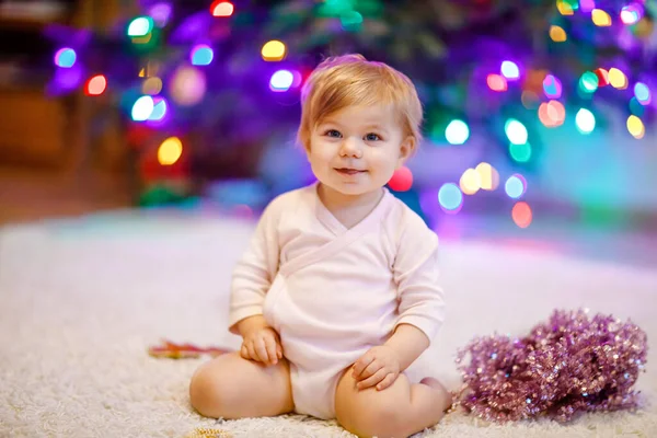 Entzückendes kleines Mädchen mit bunten Lichtergirlanden in niedlichen Händen. Kleines Kind in festlicher Kleidung schmückt Weihnachtsbaum mit Familie. Erstes Fest des traditionellen Feiertags namens Weihnachten — Stockfoto