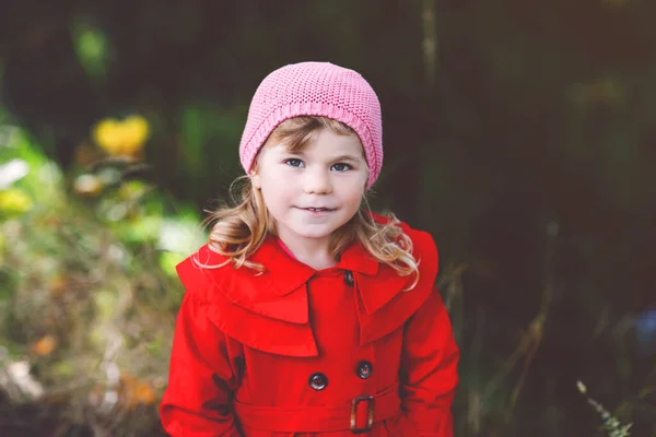 Nettes kleines Mädchen in rotem Mantel, das durch den herbstlichen Wald spaziert. Glückliches gesundes Baby, das mit seinen Eltern spazieren geht. Sonniger Herbsttag mit Kind. Aktive Freizeit und Aktivität mit Kindern in der Natur. — Stockfoto