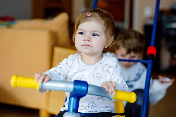 Garotinho empurrando bicicleta ou triciclo com a linda irmãzinha. Menina e irmão criança brincando juntos em casa, dentro de casa. Ligação de irmãos e amor, atividade conjunta e comum e jogo. — Fotografia de Stock