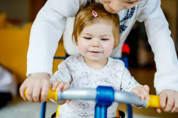 Little kid boy pushing bycicle or tricycle with cute baby sister. Toddler girl and brother playing together at home, indoors. Siblings bonding and love, jointly and common activity and game. — Stock Photo, Image