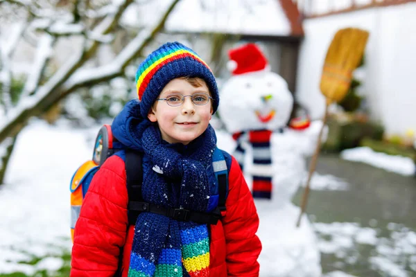 Счастливый мальчик в очках веселится со снегом по дороге в школу, в начальный класс — стоковое фото