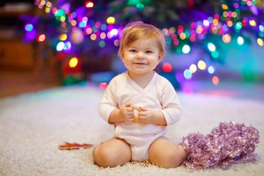 Sevimli bir kız bebek ellerinde renkli bir çelenk tutuyor. Noel ağacını aile ile süsleyen şenlikli elbiseli küçük bir çocuk. Weihnachten adlı geleneksel bayramın ilk kutlaması.