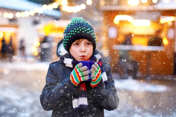 Kleine schattige jongen drinken hete kinderen punch of chocolade op de Duitse kerstmarkt. Gelukkig kind op traditionele familiemarkt in Duitsland, lachende jongen in kleurrijke winterkleding — Stockfoto