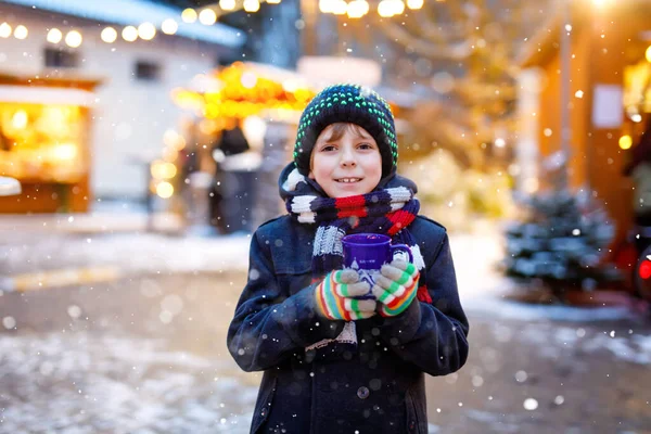 Niño lindo bebiendo ponche de niños calientes o chocolate en el mercado de Navidad alemán. Niño feliz en el mercado familiar tradicional en Alemania, niño risueño en ropa de invierno colorida — Foto de Stock