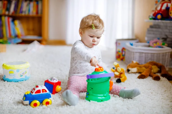 Šťastná radostná holčička hrající si s různými barevnými hračkami doma. Rozkošné zdravé batole dítě baví hrát sám. Aktivní volný čas v interiéru, školce nebo divadelní škole. — Stock fotografie