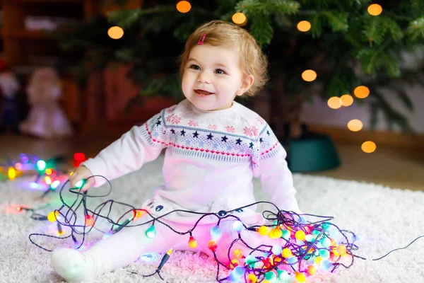 Adorable niña sosteniendo luces coloridas guirnalda en manos lindas. Niño pequeño en ropa festiva decorando el árbol de Navidad con la familia. Primera celebración de la fiesta tradicional llamada Weihnachten — Foto de Stock