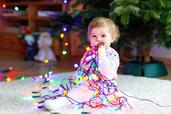 Αξιολάτρευτο κοριτσάκι κρατώντας πολύχρωμα φώτα γιρλάντα σε χαριτωμένα χέρια. Μικρό παιδί με γιορτινή ενδυμασία στολίζοντας χριστουγεννιάτικο δέντρο με οικογένεια. Πρώτη γιορτή των παραδοσιακών διακοπών που ονομάζεται Weihnachten — Φωτογραφία Αρχείου