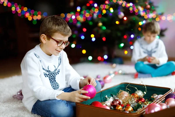 Beautiful kid boy with eye glasses and colorful vintage xmas toys and balls in old suitcase. children decorating Christmas tree — Stock Photo, Image