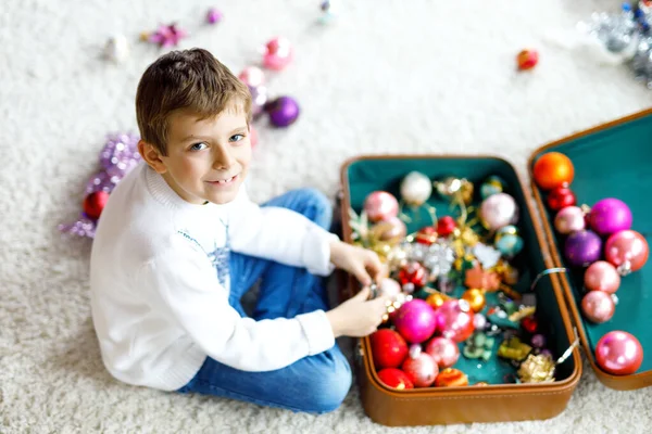 Beautiful kid boy and colorful vintage xmas toys and ball in old suitcase. Child decorating Christmas tree — Stock Photo, Image
