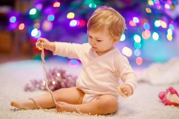 Entzückendes kleines Mädchen mit bunten Lichtergirlanden in niedlichen Händen. Kleines Kind in festlicher Kleidung schmückt Weihnachtsbaum mit Familie. Erstes Fest des traditionellen Feiertags namens Weihnachten — Stockfoto