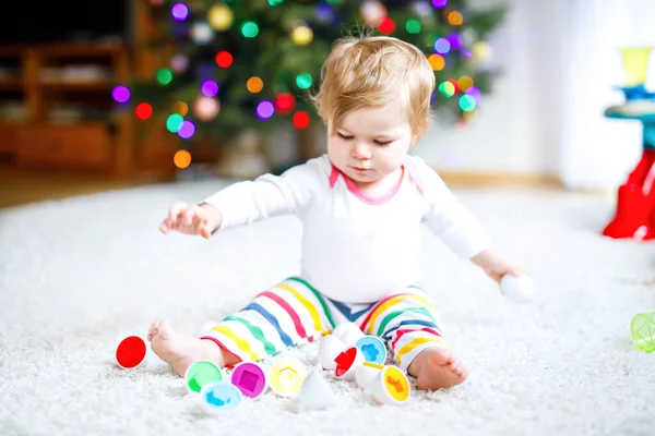 Адекватная симпатичная маленькая девочка, играющая с развивающими игрушками дома или в детском саду. Счастливый здоровый ребенок развлекается с разноцветной игрушкой-сортировщиком. Ребенок учится различным навыкам, — стоковое фото