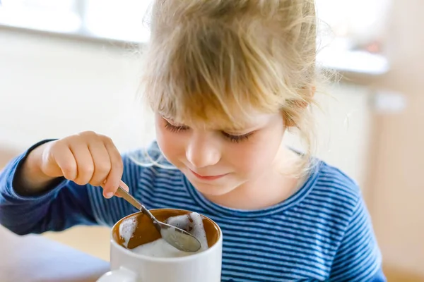 可爱的蹒跚学步的小女孩喝着有泡沫的热牛奶。在室内快乐健康的孩子，喝巧克力. — 图库照片
