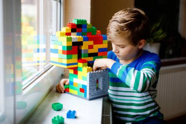 Küçük çocuk bir sürü renkli plastik blokla oynuyor. Sevimli okul çocuğu, bina inşa etmek ve bina inşa etmek konusunda çok eğleniyor. Korona zamanındaki yaratıcı eğlence teknikleri ve robotik