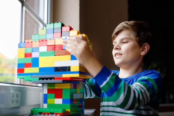 Kleine jongen die speelt met veel kleurrijke plastic blokken. Schattig schoolkind dat plezier heeft met bouwen en bouwen door raam. Creatieve vrijetijdsbesteding techniek en robottechniek tijdens corona tijd — Stockfoto