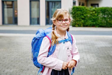 Gözlüklü ve sırt çantalı mutlu bir ilkokul öğrencisi okula giderken yolda yürüyor. Gülümseyen öğrenci okula, eğitime ve çocukluk yaşam tarzı konseptine hazır..
