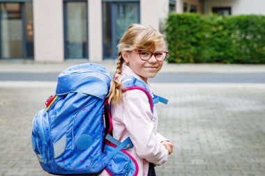 Gözlüklü ve sırt çantalı mutlu bir ilkokul öğrencisi okula giderken yolda yürüyor. Gülümseyen öğrenci okula, eğitime ve çocukluk yaşam tarzı konseptine hazır..