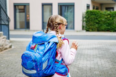 Gözlüklü ve sırt çantalı mutlu bir ilkokul öğrencisi okula giderken yolda yürüyor. Gülümseyen öğrenci okula, eğitime ve çocukluk yaşam tarzı konseptine hazır..