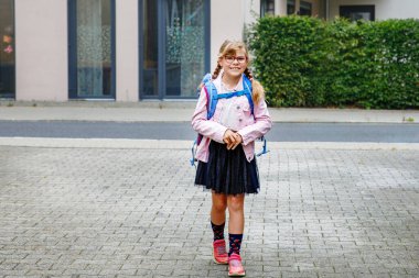 Gözlüklü ve sırt çantalı mutlu bir ilkokul öğrencisi okula giderken yolda yürüyor. Gülümseyen öğrenci okula, eğitime ve çocukluk yaşam tarzı konseptine hazır..