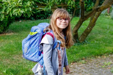 Gözlüklü ve sırt çantalı mutlu bir ilkokul öğrencisi okula giderken yolda yürüyor. Gülümseyen öğrenci okula, eğitime ve çocukluk yaşam tarzı konseptine hazır..