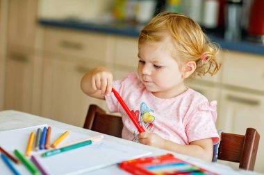 Kalemle resim yapmayı öğrenen sevimli bir bebek. Küçük çocuk renkli keçeli kalemlerle evde resim çiziyor. Evde ya da çocuk odasında renkler deneyen sağlıklı, mutlu bir kız.