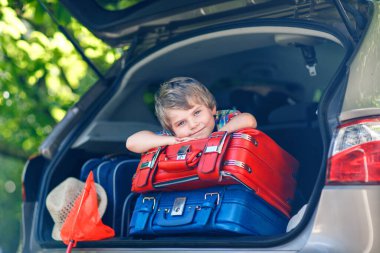 Yaz tatilinden önce ailesiyle birlikte araba bagajında oturan sevimli küçük çocuk. Bavulları ve oyuncakları olan mutlu çocuk seyahate çıkıyor, gerçek hayat, gerçek insanlar..