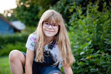 Gözlüklü, yaz akşamları açık havada gülümseyen ilkokul kızının portresi. Gerçek hayattaki otantik çocukluk anı