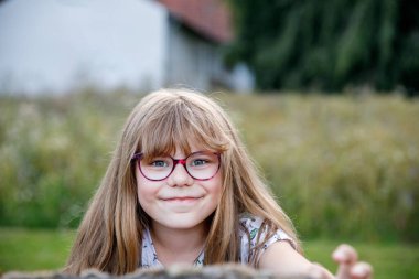 Gözlüklü, yaz akşamları açık havada gülümseyen ilkokul kızının portresi. Gerçek hayattaki otantik çocukluk anı